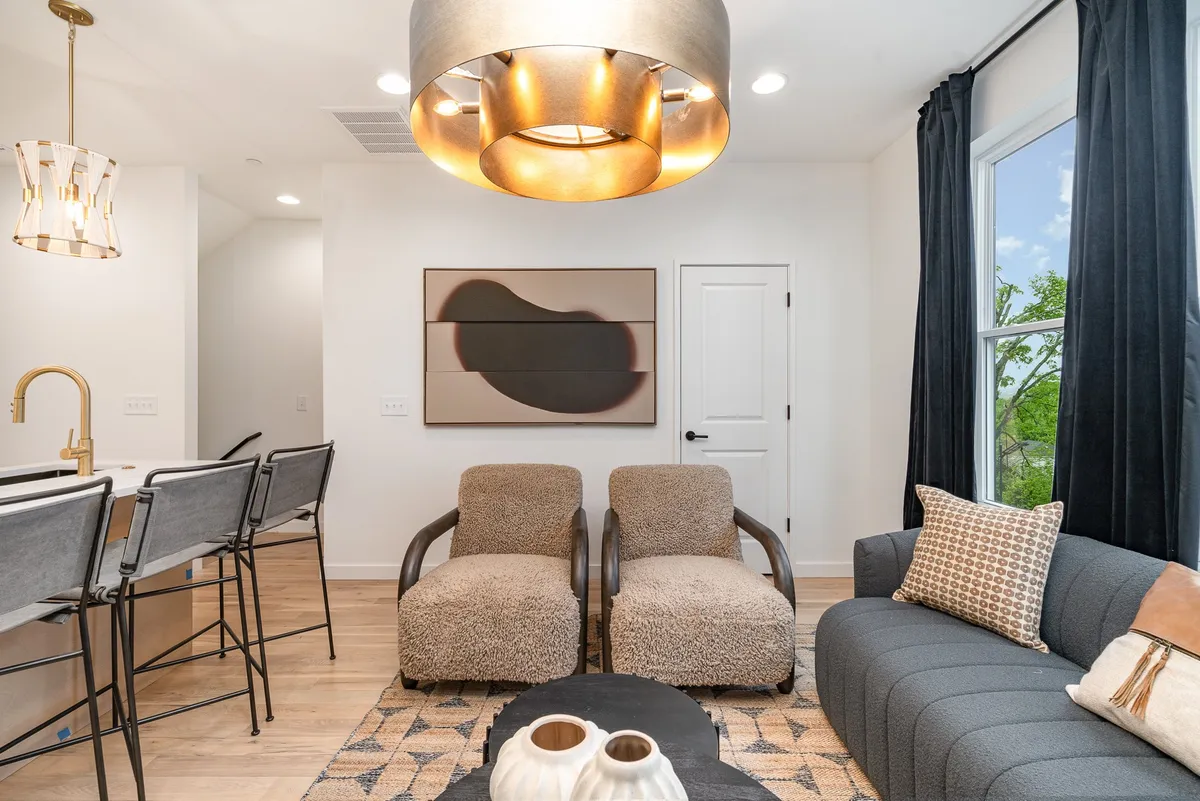A cozy seating arrangement with a chic light fixture, modern art, and textured accent pillows. The area is set up for casual gatherings, reading, or enjoying a movie, fostering an intimate, inviting mood.