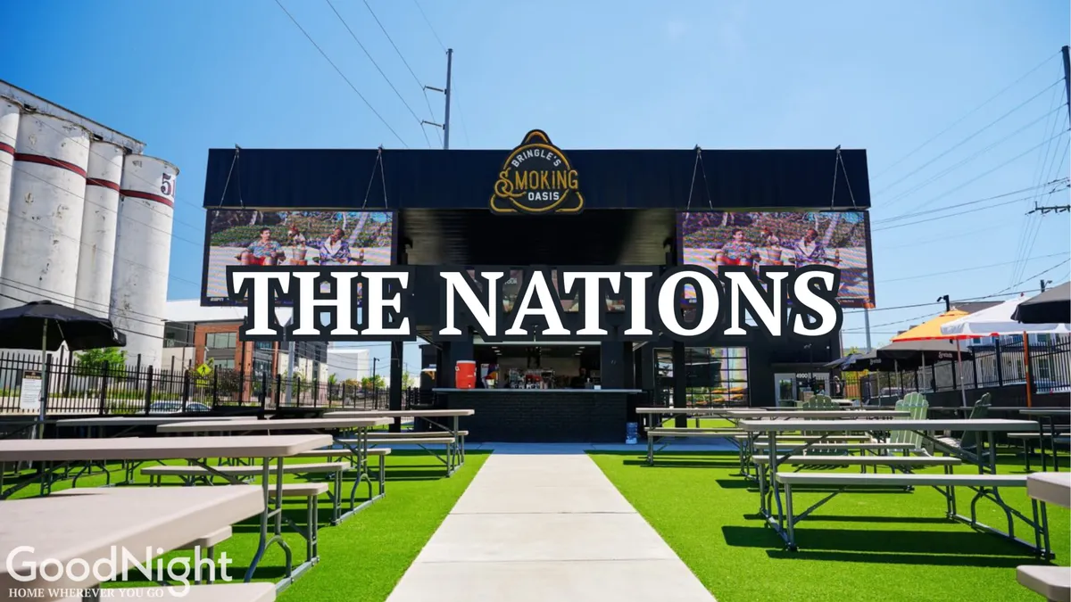 A lively exterior scene featuring large 'THE NATIONS' signage, outdoor seating areas, and a bustling food service counter. The atmosphere is social and vibrant, suggesting a thriving neighborhood known for communal events and local dining.
