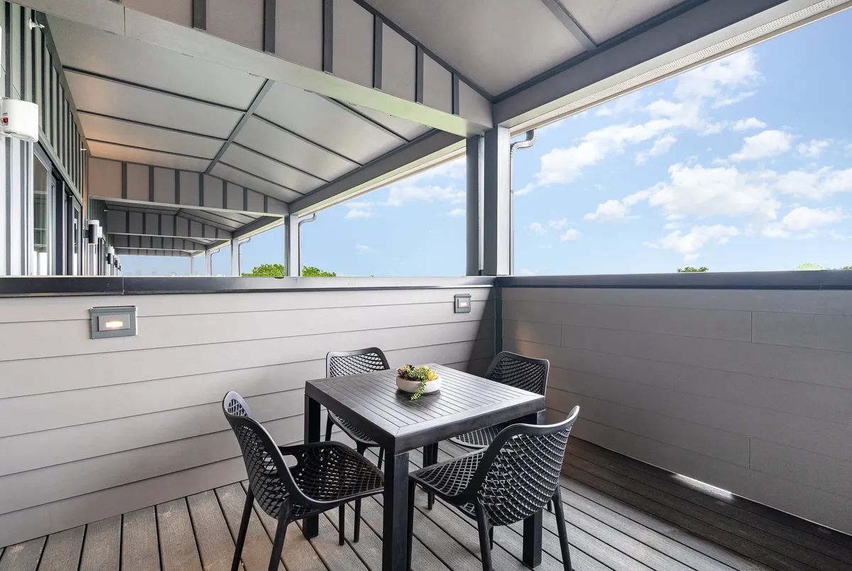 A welcoming patio area with a table adorned with plants, black woven chairs, and a covered section perfect for relaxing or informal gatherings. The space is designed for outdoor dining and casual socialization.