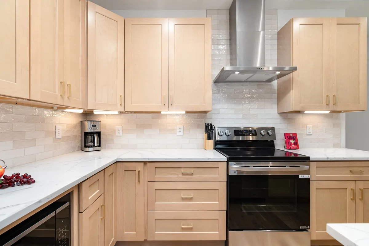 A close-up view of elegant kitchen cabinetry, a marble countertop, and premium stainless steel appliances. The space is bright and welcoming, hinting at a perfect spot for baking, preparing coffee, or setting out starter kits for guests.