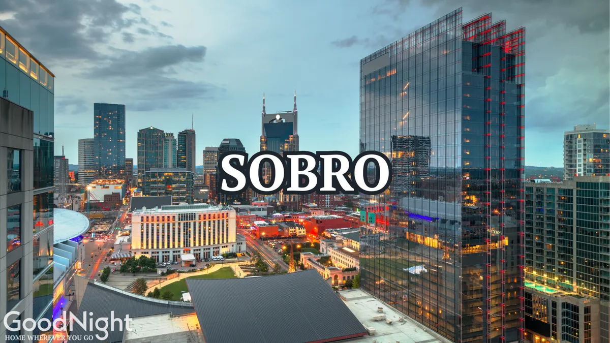 A panoramic view of Nashville’s illuminated city skyline, featuring the ‘SOBRO’ sign and twinkling lights from buildings and street scenes below. The dusk backdrop heightens the city’s dynamic nightlife appeal.