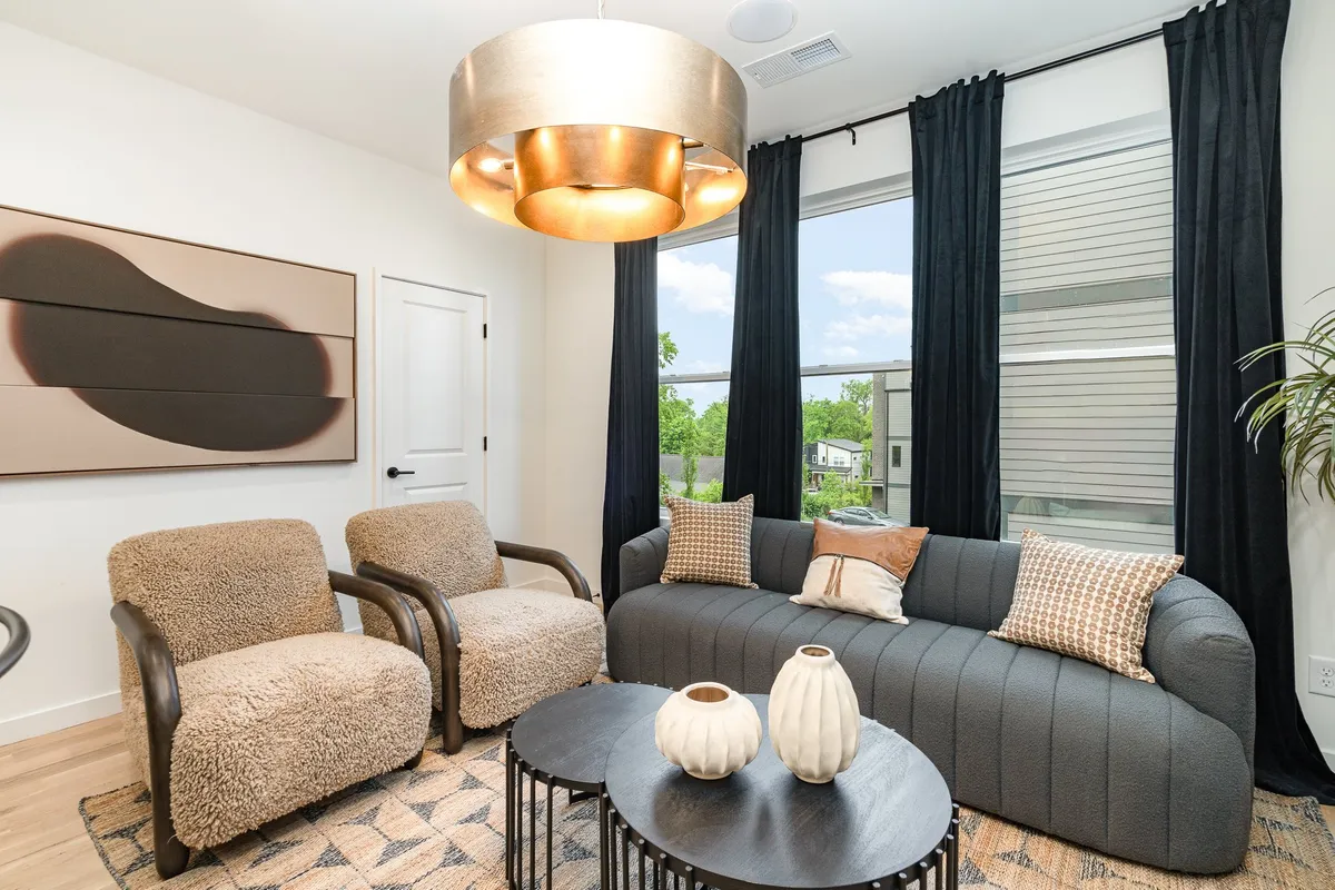 A comfortable lounge space with a large sofa, elegant chandeliers, assorted chairs, a coffee table, and curated artwork. The arrangement encourages group conversations and relaxation, while abundant natural light creates a welcoming atmosphere.