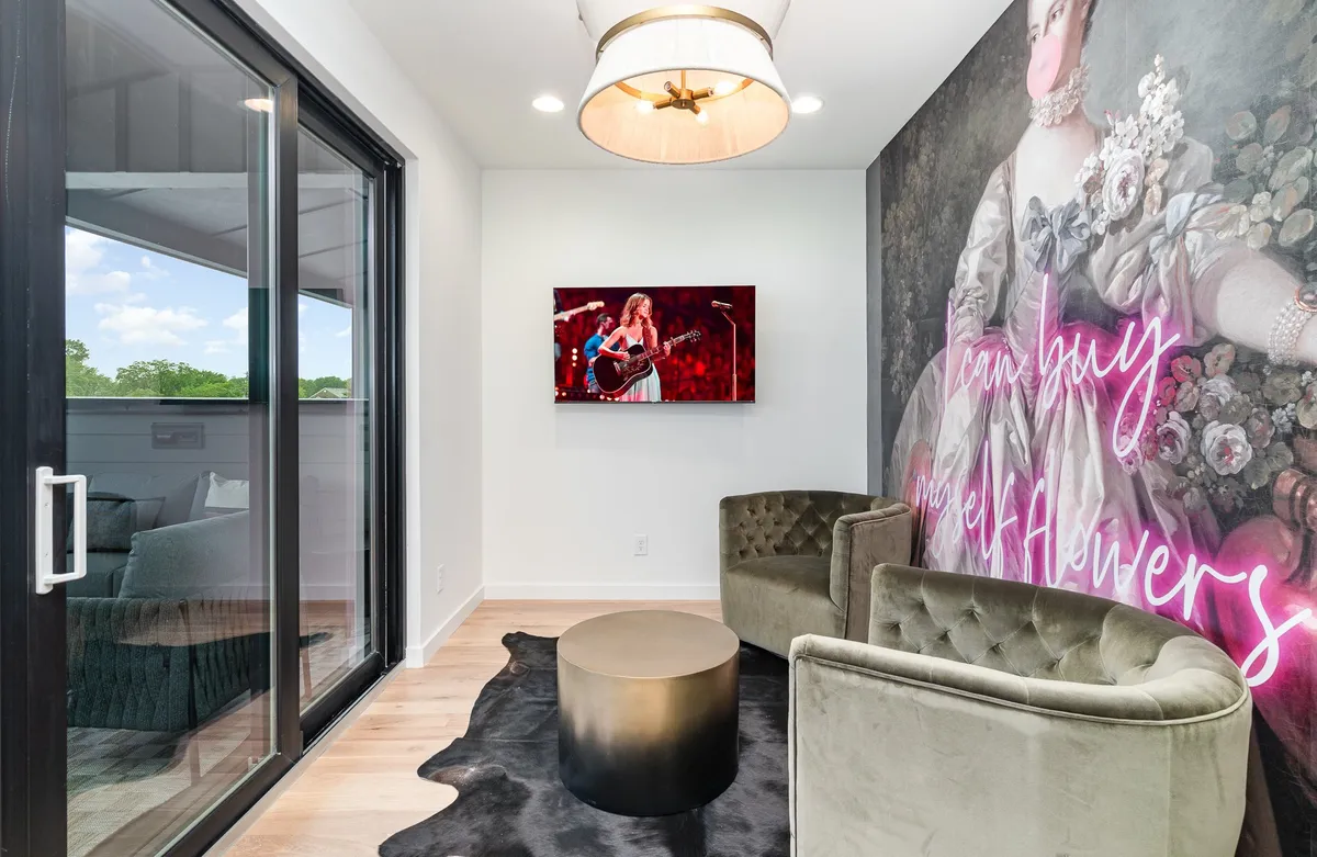 A contemporary living area featuring a vintage-style chandelier, striking bold wall art, a large television, and plush seating arranged for conversation and relaxation. The setting feels sophisticated yet comfortable, with the wall art acting as a visual centerpiece.